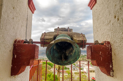 Bronze bell at old historic church against cloudy sky