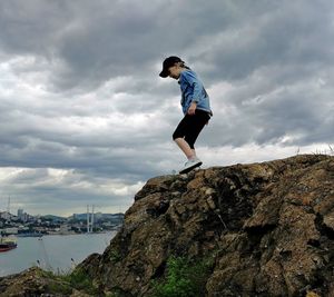 Side view of young man standing on rock against sky