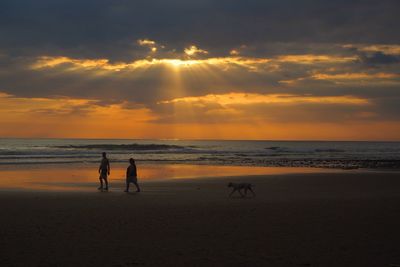 Silhouette people on beach against sky during sunset