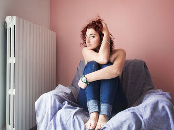 Young woman sitting on sofa by radiator at home