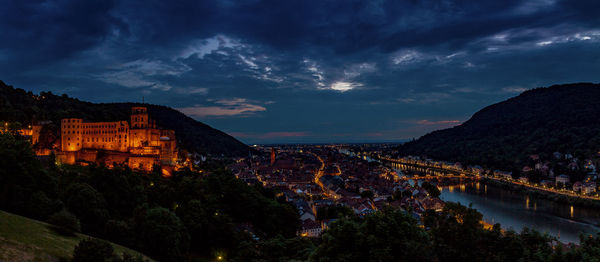 Illuminated buildings in city against cloudy sky