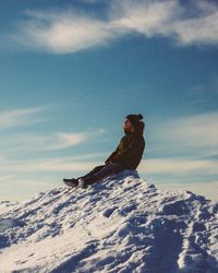 Man sitting on snow covered mountain against sky