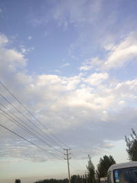 Low angle view of electricity pylon against cloudy sky