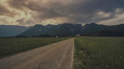 Dirt road along landscape and mountains against sky