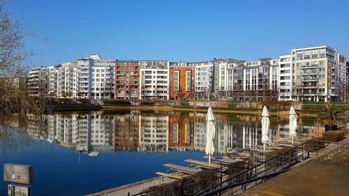 Reflection of buildings in canal against clear blue sky