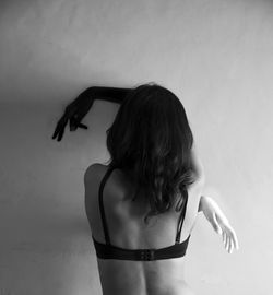 Rear view of woman wearing bra standing against wall