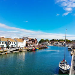 Sailboats in sea by buildings against blue sky