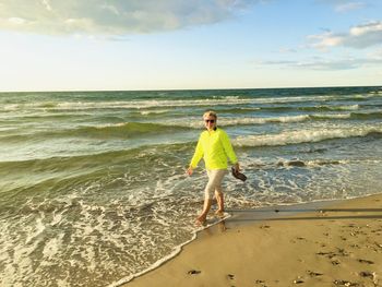 Rear view of woman walking at beach against sky