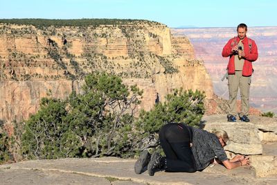 Man examining camera by female friend photographing while kneeling on mountain