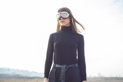 Young woman standing wearing flying goggles standing against sky