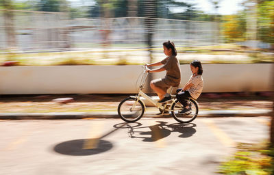 Motion blur sibling riding bicycle on road in city