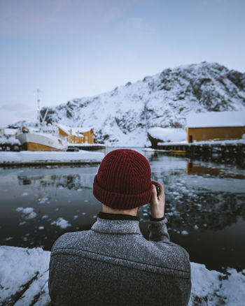 Rear view of man photographing lake while standing against sky during winter
