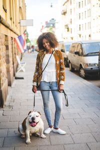 Portrait of smiling mid adult woman standing with dog on sidewalk in city