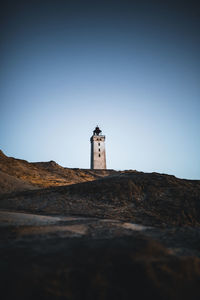 Lighthouse by building against clear blue sky