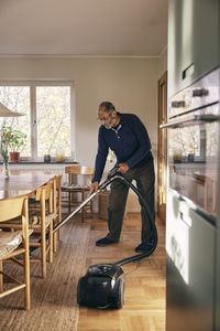 Senior man cleaning carpet with vacuum cleaner while standing at home