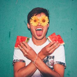 Man holding watermelon slices with eyes covered by flowers against wall