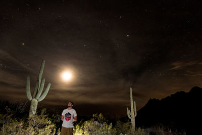 Rear view of man standing on field against sky at night