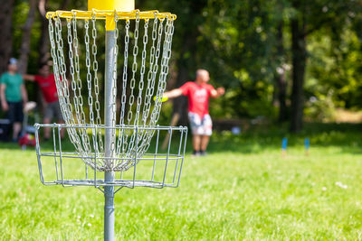 Disc golf player throwing a flying disc in the park, chain basket in the focus