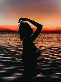 Silhouette woman standing by sea against sky during sunset