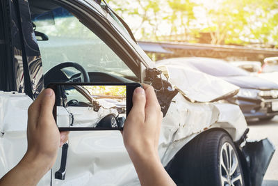 Cropped image of hand photographing damaged car through digital tablet
