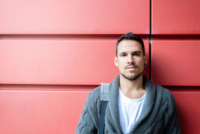 Front view of a fashionable young man standing against red wall