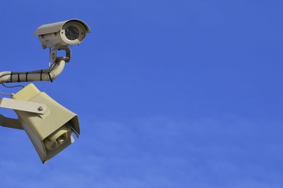 Low angle view of security camera against blue sky