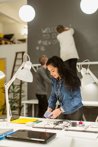 Mid adult businesswoman arranging desk against colleagues working in creative office