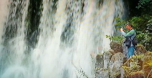 Side view of man looking at waterfall in forest