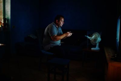 Man holding remote control against electric fan in darkroom