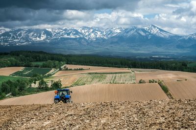 Tractor ploughing farmland on rolling hills against a mountain backdrop