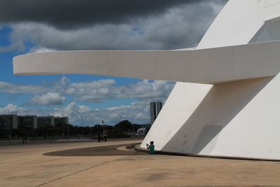 Man sitting near building against cloudy sky