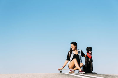 Woman with dog and skateboard against clear blue sky