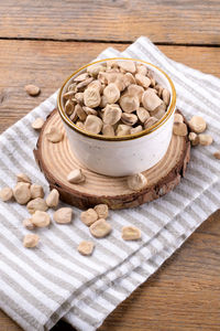 Dry raw cicerchia or indian pea on a ceramic bowl with napkin on wooden background, close up