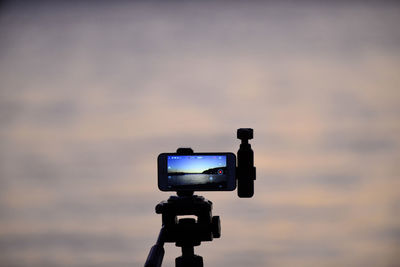 Close-up of camera photographing against sky during sunset
