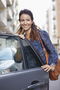 Businesswoman with bag standing by open car door on street