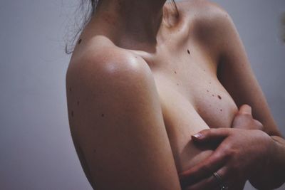 Midsection of shirtless woman covering breast with hands at home