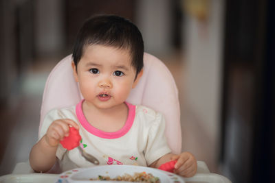 Cute baby girl eating food at home