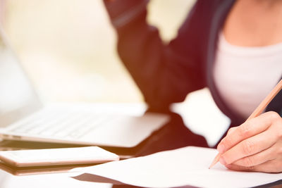 Midsection of businesswoman writing in book at office