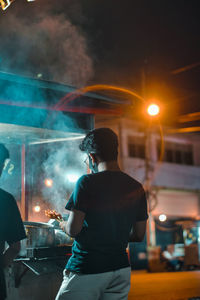 Rear view of man standing on illuminated street at night