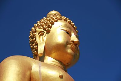 Low angle view of buddha statue against clear blue sky