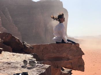 Woman sitting on rock against sky