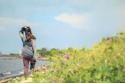 Woman standing on field by flowering plants against sky