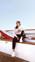 Full length of thoughtful young woman looking away while sitting on ship against clear sky