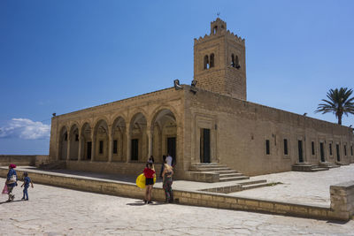 People in front of historic building against blue sky