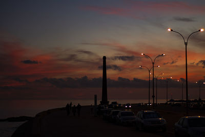 Cars on street by sea against sky during sunset