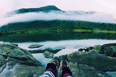 Low section of man standing by lake against mountain