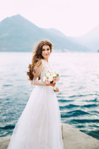 Full length portrait of woman with bouquet standing against lake