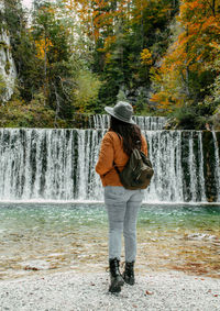 Full length rear view of woman standing in front of waterfall