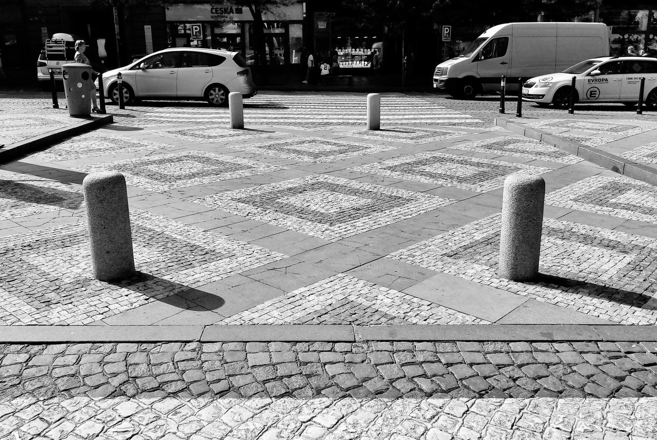 motor vehicle, city, car, mode of transportation, transportation, architecture, street, land vehicle, cobblestone, footpath, road, day, built structure, building exterior, sign, no people, outdoors, zebra crossing, stone, post, paving stone