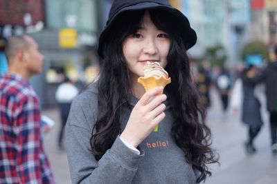 Portrait of smiling woman holding ice cream on street in city